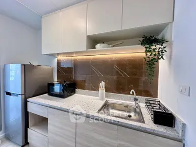 Modern kitchen with sleek design and appliances, featuring a fridge, microwave, and stylish backsplash.