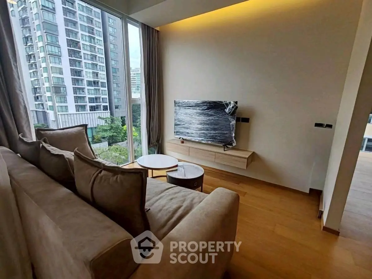 Modern living room with large windows and city view, featuring a cozy sofa and sleek TV setup.