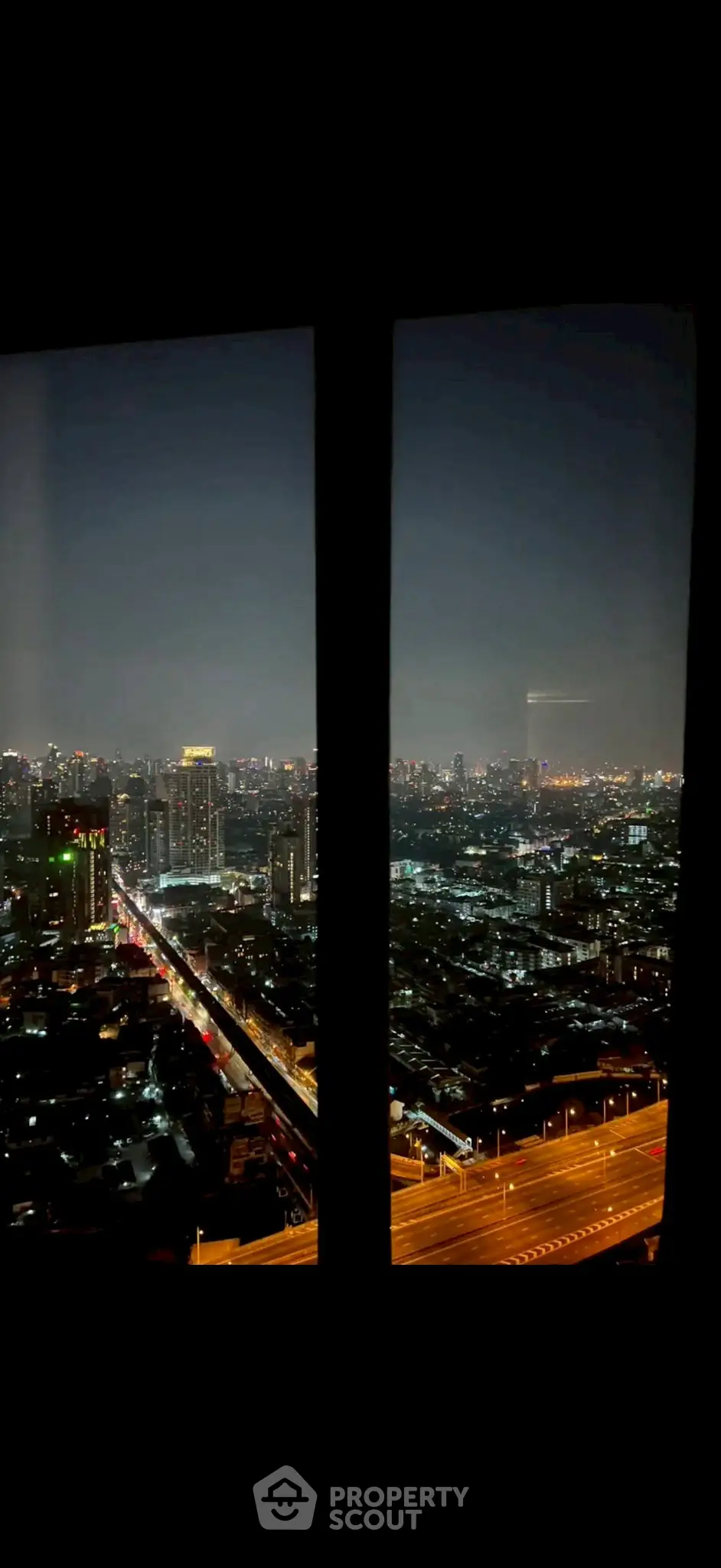 Stunning cityscape view from high-rise window at night with vibrant city lights.