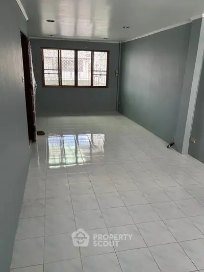 Spacious empty living room with tiled flooring and large windows for natural light.