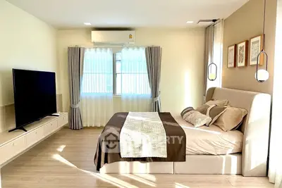 Modern bedroom with stylish decor, large TV, and natural light through window.
