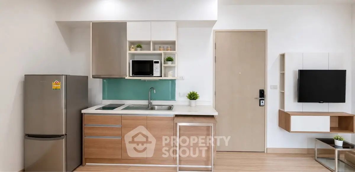 Modern kitchen with sleek cabinetry, stainless steel fridge, and wall-mounted TV in a stylish apartment.