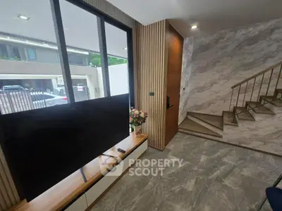 Modern living room with stylish decor and large TV, featuring elegant staircase and natural light.