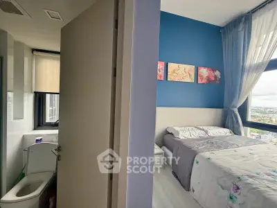Modern bedroom with blue accent wall and city view, adjacent to a compact bathroom.