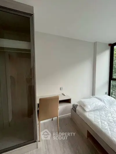 Modern bedroom with minimalist design, featuring a bed, desk, and large window for natural light.
