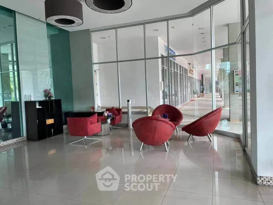 Modern lobby with stylish red chairs and glass walls in a contemporary building.