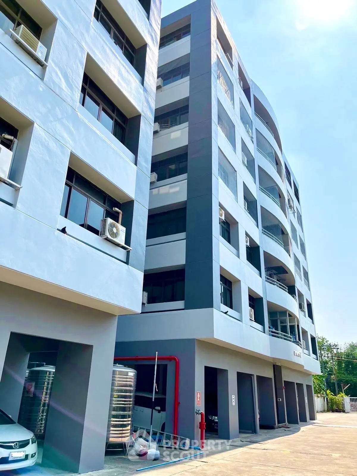 Modern multi-story residential building with sleek design and ample parking space.