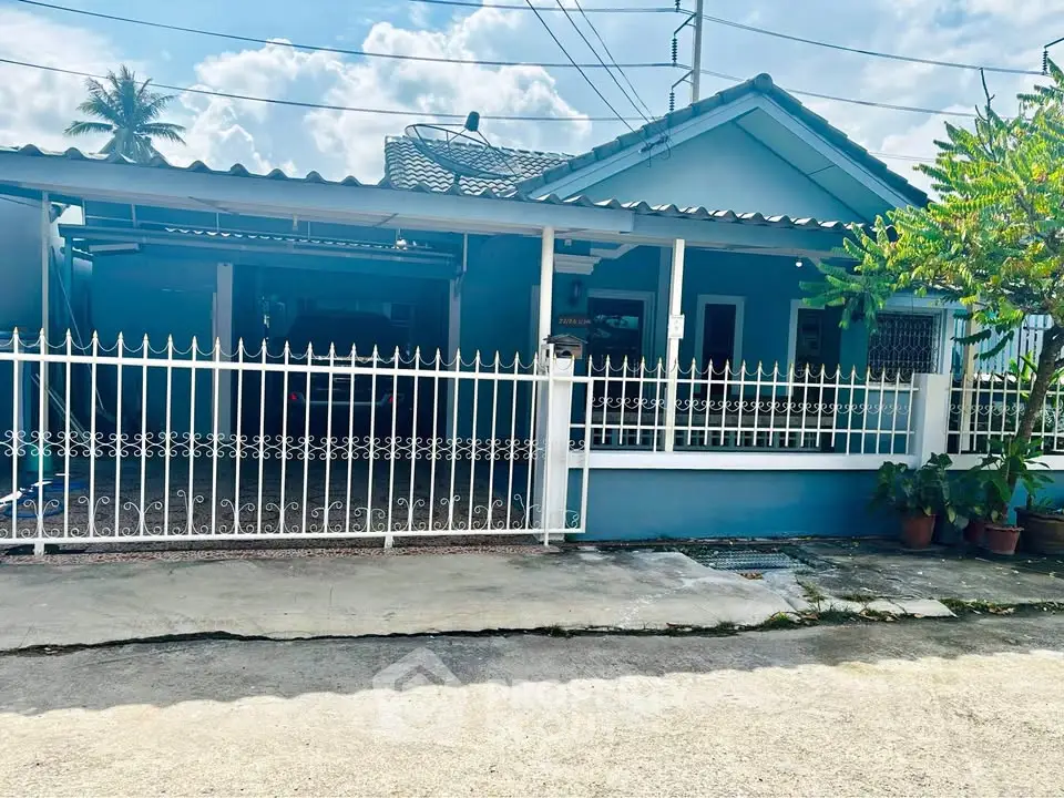 Charming blue single-story house with gated driveway and lush greenery.