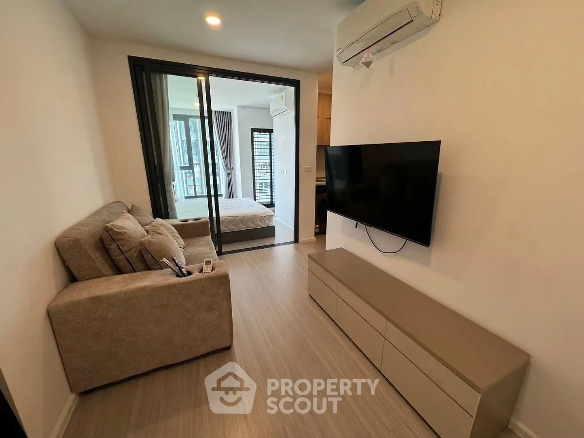 Modern living room with wall-mounted TV and cozy sofa, leading to a stylish bedroom with glass partition.