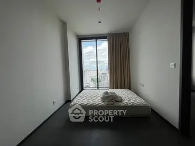 Spacious bedroom with large window offering stunning city view, featuring minimalist decor and natural light.