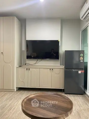 Modern living room with sleek cabinetry and flat-screen TV, featuring a compact refrigerator and stylish round table.