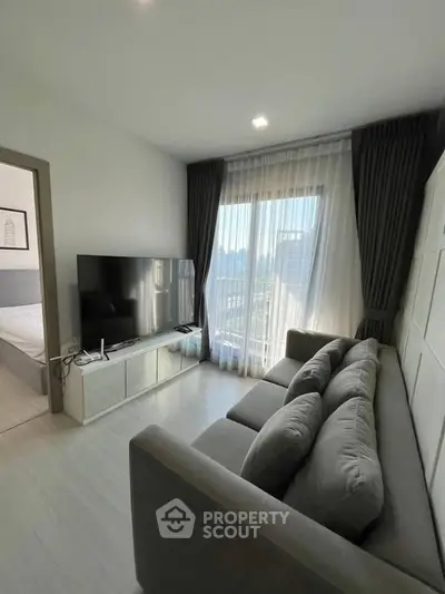 Modern living room with sleek furniture and large TV, featuring a bright window view.