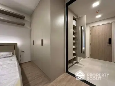 Sleek modern bedroom with built-in wardrobe and mirrored sliding doors leading to a well-lit, spacious walk-in closet, offering a blend of comfort and style.