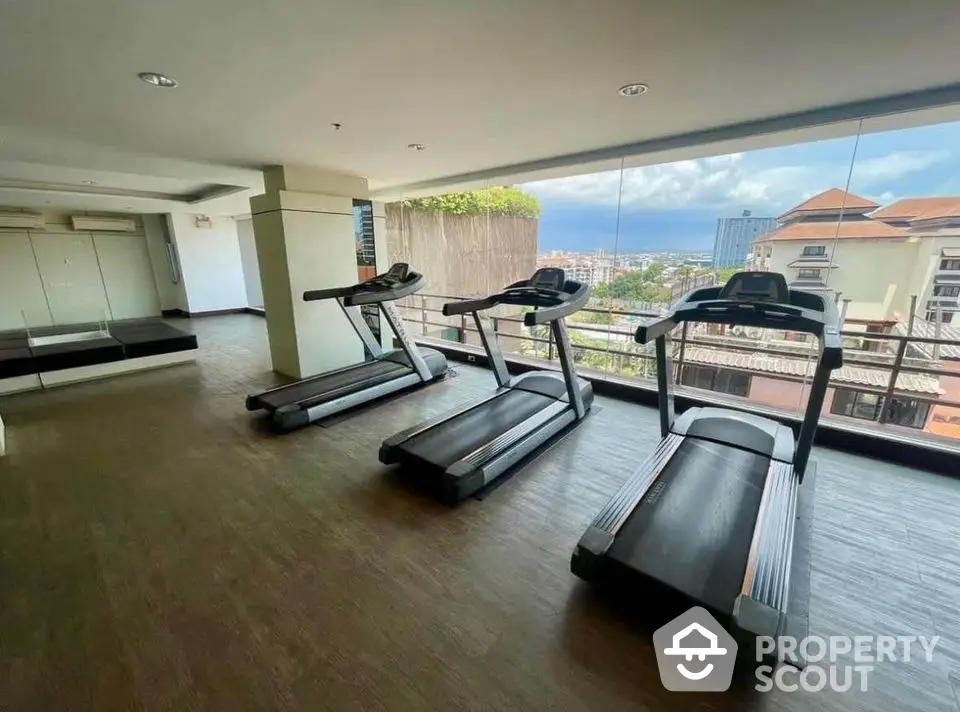 Spacious gym with modern treadmills and panoramic city view through large windows.