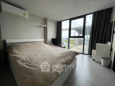 Modern bedroom with large window offering city view, featuring sleek furniture and neutral tones.