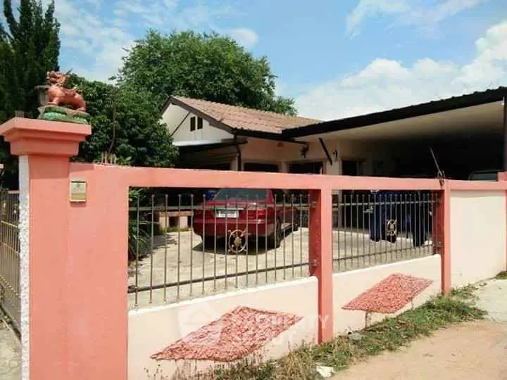 Charming single-story home with red car parked in driveway, surrounded by pink fence and lush greenery.