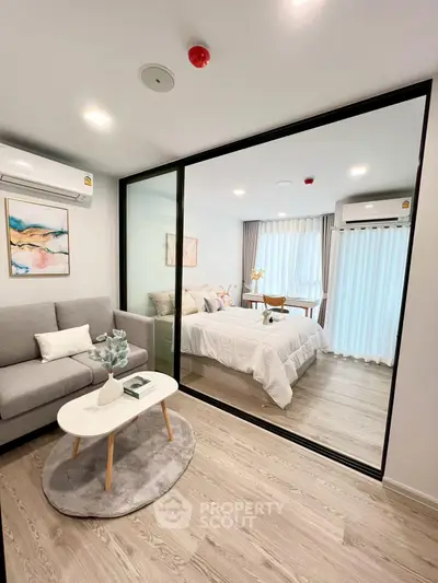 Modern apartment with glass partition separating living room and bedroom, featuring stylish decor.