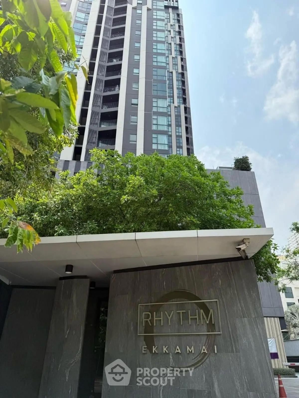 Modern high-rise building with lush greenery at Rhythm Ekkamai entrance