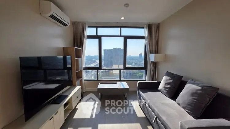 Modern living room with large windows and city view, featuring a sleek sofa and entertainment center.