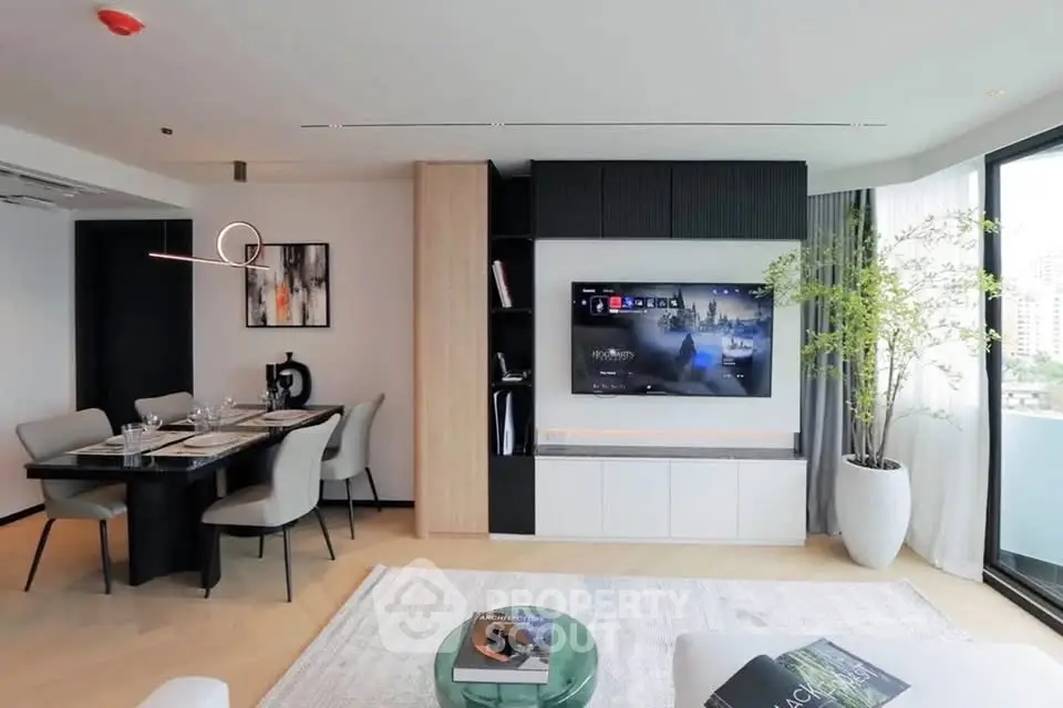 Modern living room with open layout, stylish dining area, and large TV, featuring elegant decor and natural light.