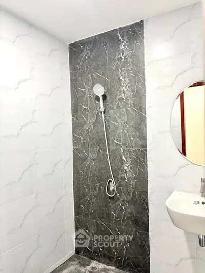 Modern bathroom with elegant marble shower wall and sleek white sink.