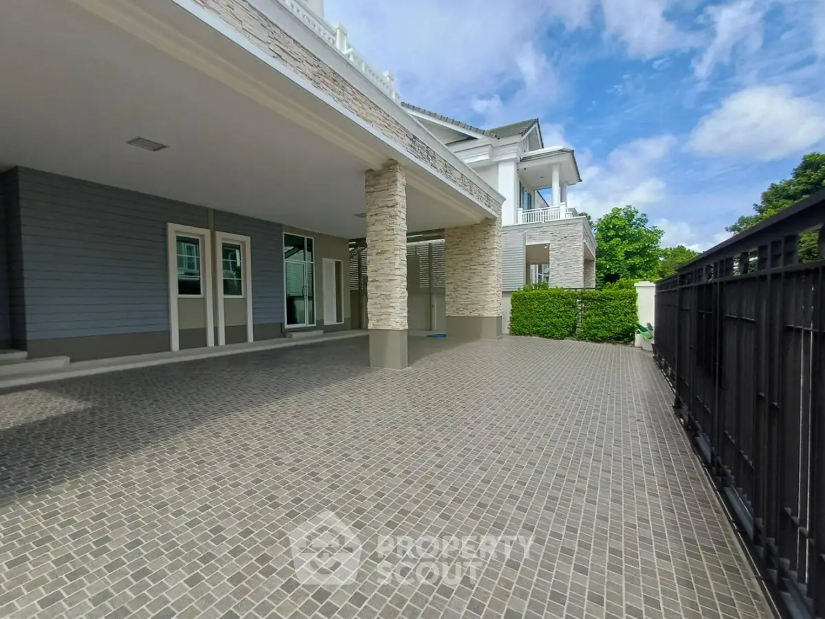 Spacious driveway of a modern luxury home with elegant stone pillars and lush greenery.