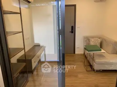 Modern living room with sleek furniture and wooden flooring, featuring a glass partition and air conditioning.