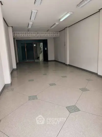 Spacious empty interior space with tiled flooring and fluorescent lighting, ideal for commercial use.