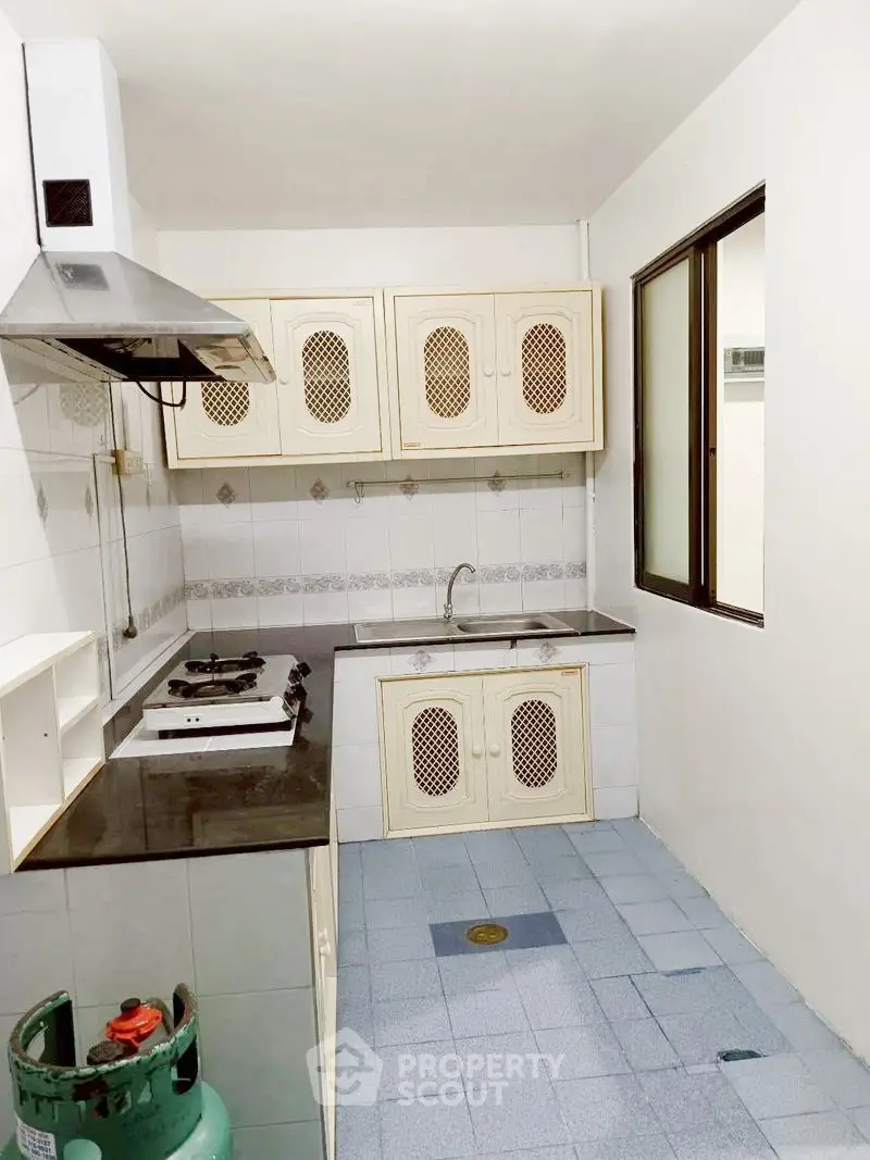 Compact kitchen with gas stove and white cabinets in cozy apartment.