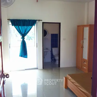 Bright and airy bedroom with gleaming tiled floors, featuring an en-suite bathroom, large windows with blue curtains, and ample storage space.