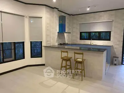 Modern kitchen with open layout and sleek design featuring bar stools and large windows.
