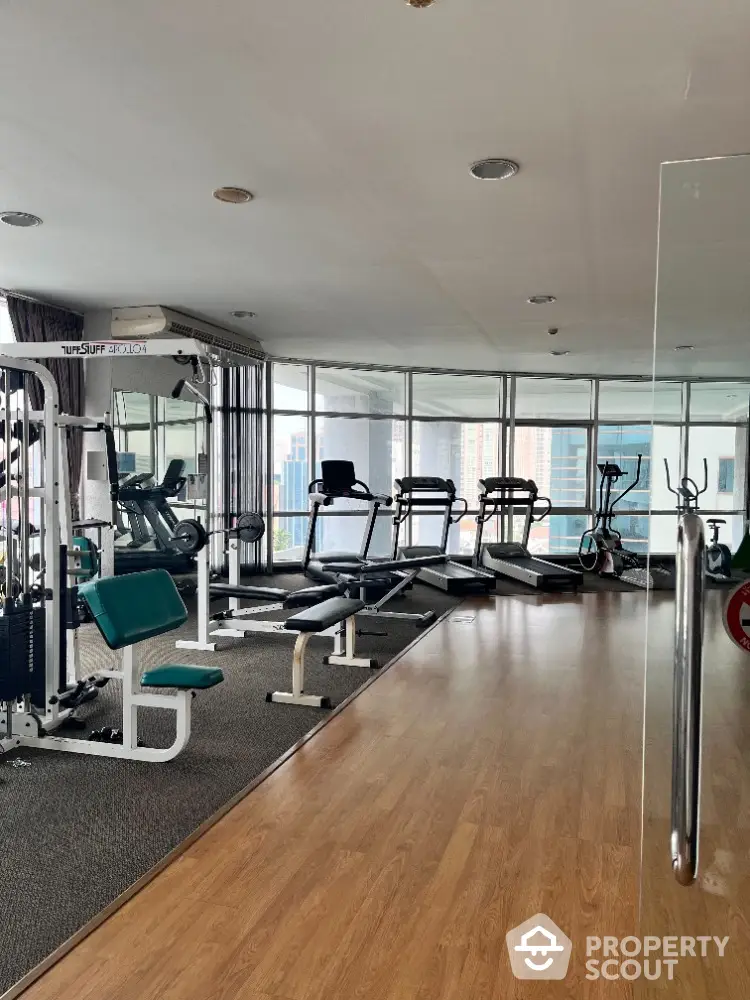 Spacious gym with modern equipment and city view in luxury apartment building.