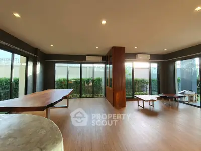 Spacious modern living room with large windows and wooden furniture, offering a serene garden view.