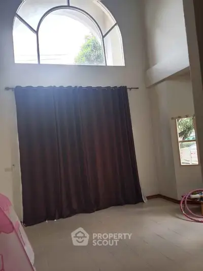 Spacious room with high ceiling and large arched window, perfect for natural light.