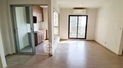 Modern apartment with open living room and kitchen, featuring large windows and wooden flooring.