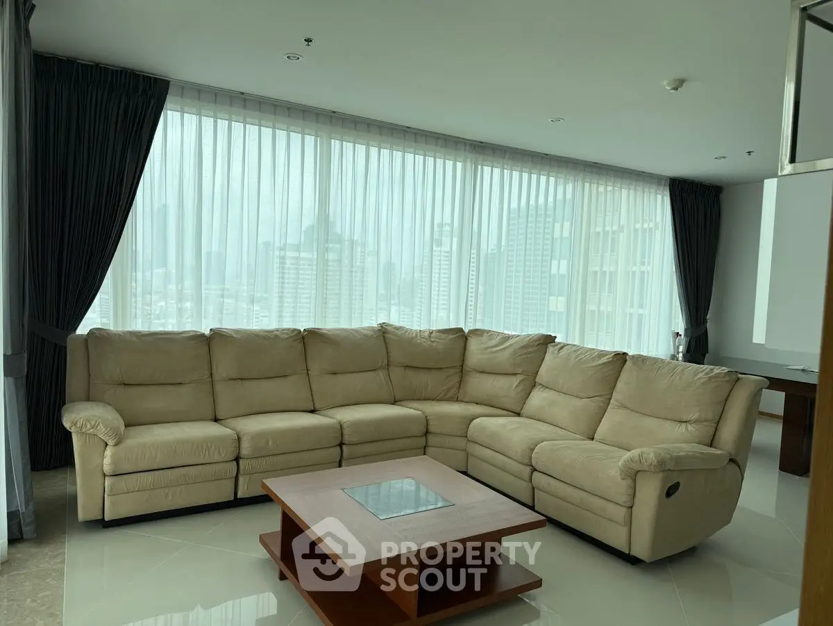 Spacious living room with large sectional sofa and city view through floor-to-ceiling windows.