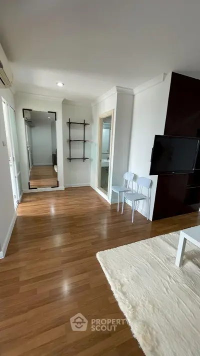 Spacious living room with modern decor and wooden flooring, featuring a cozy rug and wall-mounted TV.