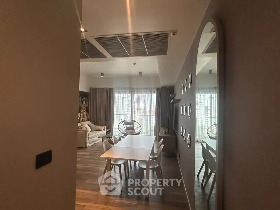 Modern living room with dining area and stylish decor, featuring large windows and contemporary furniture.