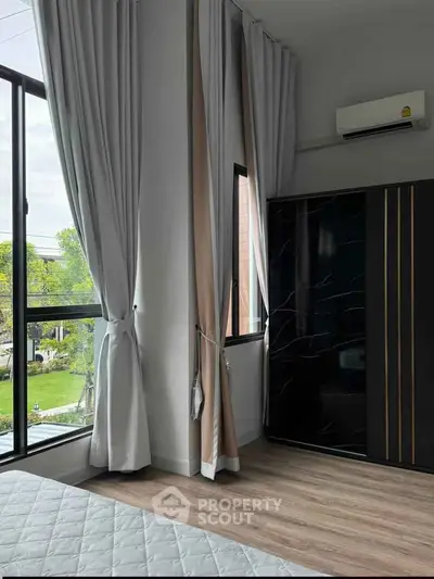 Modern bedroom with large windows, elegant curtains, and sleek wardrobe overlooking a lush garden view.
