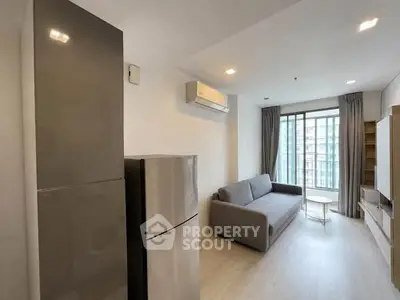 Modern living room with sleek furniture and large window offering city views.