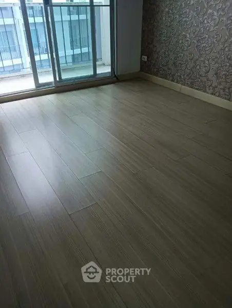 Spacious empty room with wooden flooring and large window for natural light.