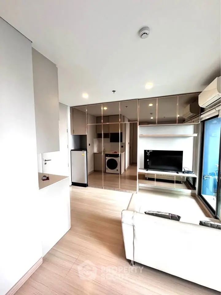 Modern living room with sleek design, featuring mirrored walls, a washing machine, and a compact kitchen area.