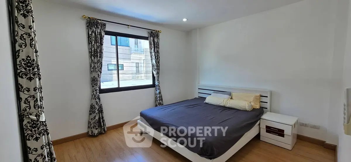 Spacious bedroom with elegant curtains and modern furnishings in a well-lit apartment.