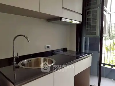 Modern kitchen with sleek black countertop and stainless steel sink in a contemporary apartment.