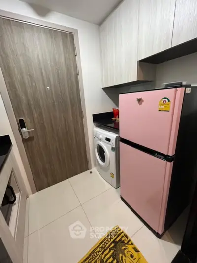 Compact kitchen with pink fridge and washing machine in modern apartment
