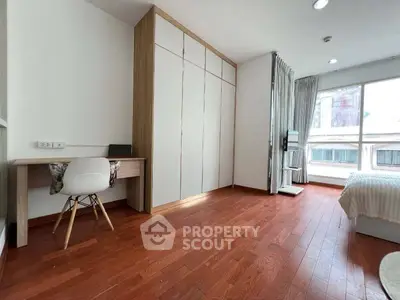 Spacious bedroom with wooden flooring, large window, and built-in wardrobe in modern apartment.