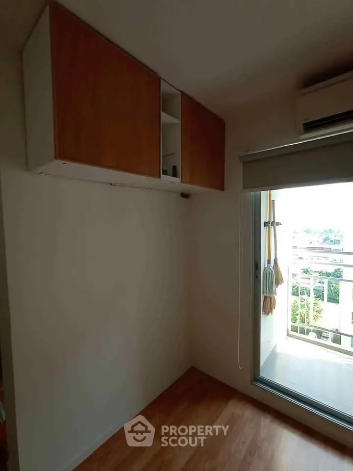 Compact room with wooden flooring, wall-mounted cabinets, and balcony access.