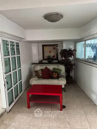 Cozy interior space with white sofa, red table, and decorative plants, perfect for relaxation.
