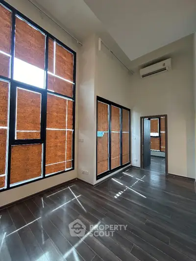 Spacious modern room with high ceilings and large windows featuring wooden blinds.
