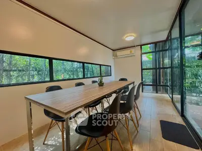 Modern dining room with large windows and garden view, featuring sleek black chairs and wooden table.